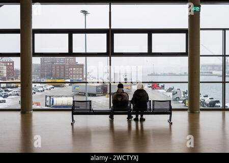 Ein Mann und eine Frau auf einer Sitzbank im Terminalgebäude der Stena Line auf das Panorama des Kieler Hafens blickend Stockfoto