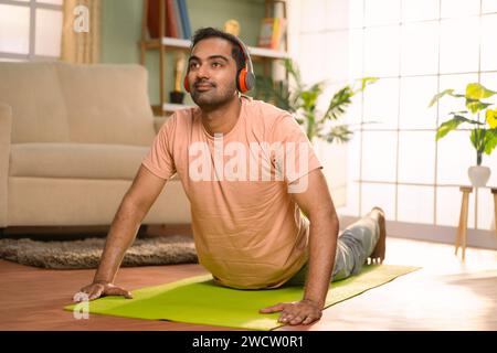 Junger indischer Mann, der Bewegung macht, indem er zu Hause Lieder auf Kopfhörern hört - Konzept von Fitness, gesundem Lebensstil und Unterhaltung Stockfoto