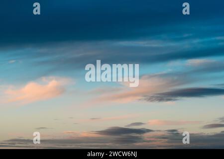 Zarte Wolken, beleuchtet durch sanftes rosafarbenes Sonnenuntergangslicht unter düsteren dunkelblauen Wolken Stockfoto