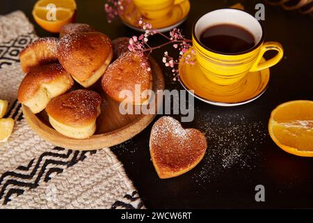 Ästhetische Teezeit mit gelben Tassen und hausgemachten herzförmigen Muffins. Cupcakes mit Orangengeschmack zum Valentinsfrühstück Stockfoto