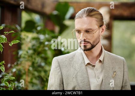 Gut aussehender eleganter Mann mit gesammelten Haaren in Brille in schickem modischem Anzug, der attraktiv posiert Stockfoto