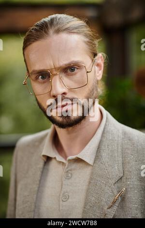 Attraktiver eleganter Anführer mit gesammelten Haaren in Brille in schickem, modischem Anzug, der attraktiv posiert Stockfoto