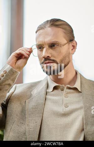 Attraktiver Anführer mit gesammelten Haaren in einer Brille in einem schicken, raffinierten Anzug, der attraktiv posiert Stockfoto