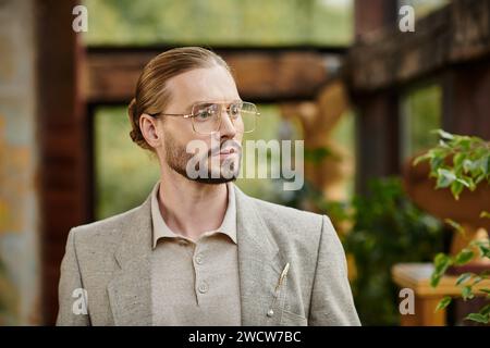 Schöner eleganter Mann mit gesammelten Haaren in Brille in schickem modischem Anzug, der attraktiv posiert Stockfoto