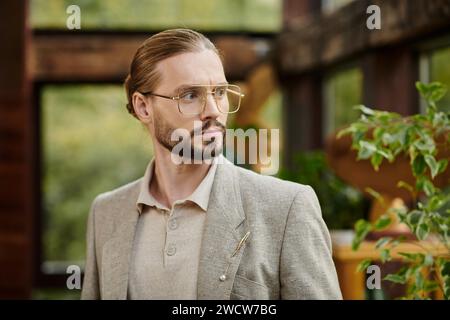 Ansprechender eleganter Anführer mit gesammelten Haaren in Brille in schickem modischem Anzug, der attraktiv posiert Stockfoto