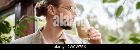 Hübscher, fokussierter Mann mit Bart und gesammelten Haaren in elegantem Anzug, der seinen heißen Kaffee trinkt, Banner Stockfoto