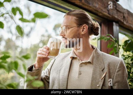 Gut aussehender ansprechender Mann mit Bart und gesammelten Haaren in elegantem Anzug, der seinen heißen Kaffee trinkt Stockfoto