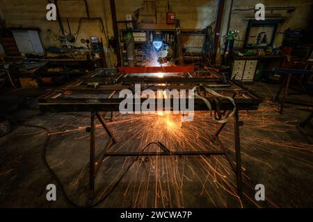 Ein Schweißer, der in einem Metallverarbeitungsunternehmen arbeitet, schweißt Eisenstangen mit vielen Funken Stockfoto