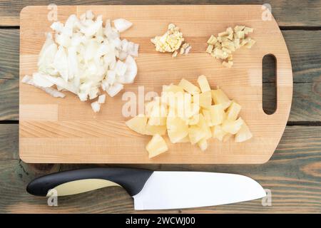 In Scheiben geschnittene Zwiebeln mit Knoblauch und Ingwer mit Ananas auf einem Schneidebrett und einem Küchenmesser. Hausmannskost. Stockfoto