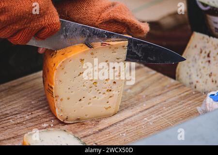 Hände einer Frau, die mit einem Messer ein Stück selbstgemachten Bio-natürlichen lettischen Käse auf einem Straßenmarkt schneidet Stockfoto