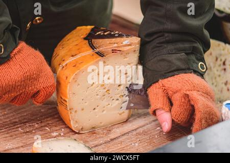 Hände einer Frau, die mit einem Messer ein Stück selbstgemachten Bio-natürlichen lettischen Käse auf einem Straßenmarkt schneidet Stockfoto