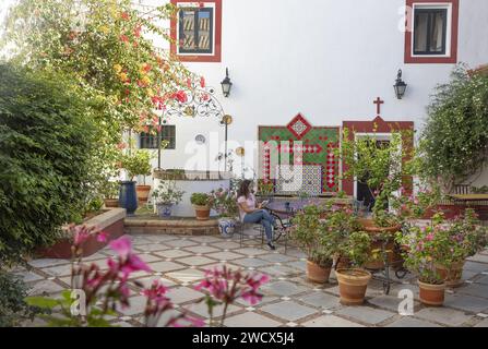 Spanien, Andalusien, Moron de la Frontera, Hacienda las Alcabalas, Frau, die an einem zellige Tisch auf dem mit Blumen geschmückten Innenhof liest, dekoriert mit Azulejos einer Hacienda im andalusischen Sevillanischen Stil Stockfoto