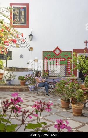 Spanien, Andalusien, Moron de la Frontera, Hacienda las Alcabalas, Frau, die an einem zellige Tisch auf dem mit Blumen geschmückten Innenhof liest, dekoriert mit Azulejos einer Hacienda im andalusischen Sevillanischen Stil Stockfoto