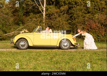 Lustige, ungewöhnliche, stilvolle, originelle Fotos mit Rollenumkehr eines jungen, attraktiven Brautpaares mit wunderschönen Veteranenautos in der Natur. Stockfoto