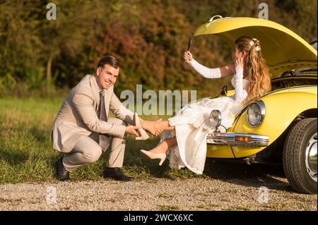 Lustige, ungewöhnliche, stilvolle, originelle Fotos mit Rollenumkehr eines jungen, attraktiven Brautpaares mit wunderschönen Veteranenautos in der Natur. Stockfoto