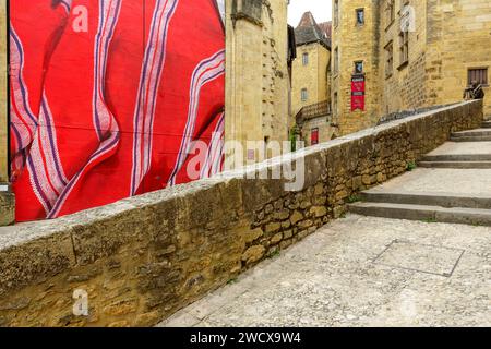 Frankreich, Dordogne, Perigord Noir, Dordogne Valley, Sarlat la Caneda, zeitgenössische Kunst namens Notre Linge (unsere Wäscherei) von stella und PITR an der Tür der ehemaligen Kirche St. Maria, die im 14. Jahrhundert erbaut wurde, heute der überdachte Markt, im Hintergrund Bronzestatue Le Badaud von Gerard Auliac und die Fassaden der ehemaligen Herrenhäuser Hotel de Vassal aus dem 15. Jahrhundert und Manoir de Gisson aus dem 13. Jahrhundert, die sich im historischen Zentrum befinden, das von der UNESCO zum Weltkulturerbe erklärt wurde Stockfoto