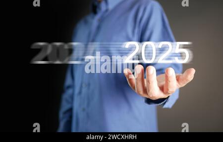 Frohes neues Jahr 2025. Die Hand eines Geschäftsmannes hält sich an einem Wechsel von 2024 in 2025, um das kommende Jahr der neuen Geschäftsreise zu begrüßen. Stockfoto