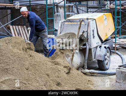 Sotschi, Russland - 23. Februar 2023: Ein Arbeiter lädt Sand in eine halbtrockene Estrichmaschine Stockfoto