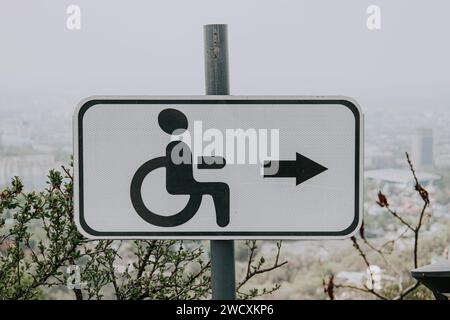 Weißes Straßenschild für Menschen mit Behinderungen, Behinderungen, mit schwarzer Ikone Mann im Rollstuhl und Rechtspfeil. Barrierefreie Umgebung im städtischen Raum. Stockfoto