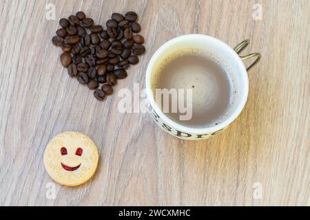 Eine Tasse Kaffee, ein lächelnder Keks und Kaffeebohnen in Herzform Stockfoto