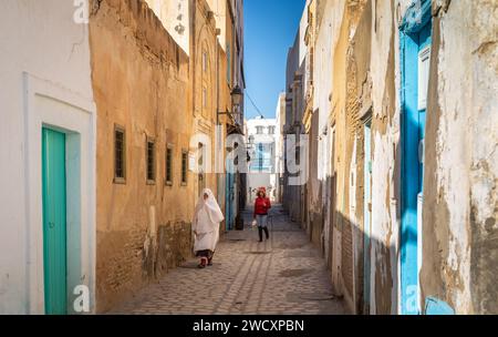 Eine ältere Tunesierin in einem traditionellen Foutah und eine junge moderne Frau gehen in der alten Medina von Kairouan in Tunesien eine Gasse entlang. Kair Stockfoto