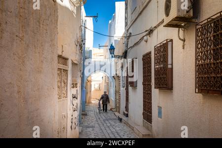 Ein Tunesier schiebt sein Fahrrad durch eine enge Gasse in der alten Medina von Kairouan in Tunesien. Kairouan ist die 4. Heiligste Stadt im Islam und Stockfoto