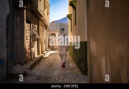 Eine ältere Tunesierin in einem traditionellen Foutah geht eine enge Gasse in der alten Medina von Kairouan in Tunesien entlang. Kairouan ist der 4 Stockfoto