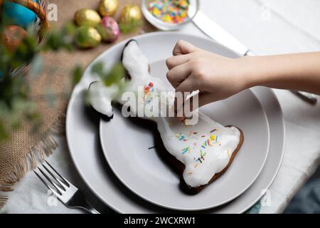 Hand des Kindes, die gebackenen Osterhasen-Lebkuchenkeks mit mehrfarbigen Zuckerstreuseln dekoriert Stockfoto