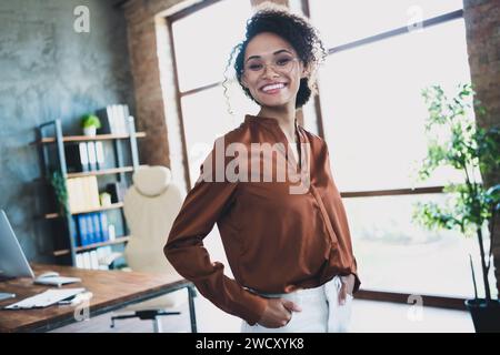 Porträt einer positiven hübschen repräsentativen Dame, die Handtaschen, die ein zahnloses Lächeln posieren, geräumiger, moderner Arbeitsplatz im Inneren Stockfoto