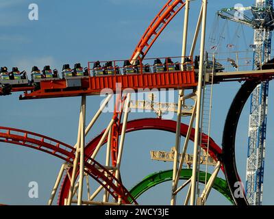 München, Oktoberfest Skyline: Wagen der Olympischen Ringachterbahn in Bewegung und im Hintergrund der Kettenflieger Bayern Turm von 97 Metern Stockfoto
