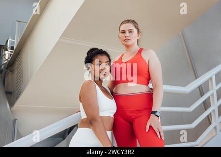 Porträt zweier übergroßer Frauen in Fitnesskleidung mit Blick auf die Kamera. Zwei große Athleten stehen nach dem Workout im Freien zusammen und entspannen sich. Stockfoto