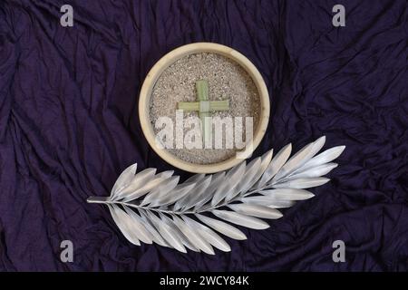 Asche, Kreuz und silbernes Palmenblatt auf violettem Hintergrund. Ash Wednesday-Konzept. Stockfoto