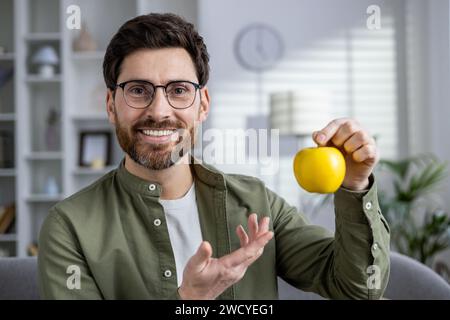 Porträt eines Reifen Mannes zu Hause, der einen Apfel in der Hand hält, lächelt und in die Kamera blickt, Nahaufnahme. Stockfoto