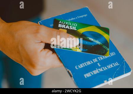 In dieser Abbildung ist die Hand zu sehen, die die Auxílio Brasil-Karte (Bolsa Família) und Carteira de Trabalho e Previdência Social hält. Stockfoto