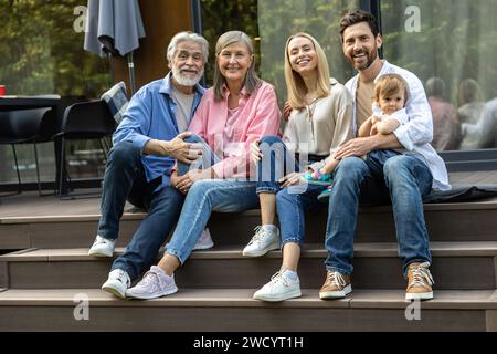 Glückliche große Familie, die auf den Stufen des Hauses sitzt Stockfoto