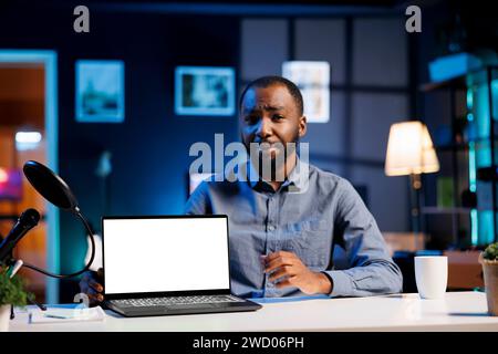 afroamerikanischer Tech-Experte präsentiert Modell-Laptop in der Einstiegsklasse für niedrige Budgets. Viraler Content Creator überprüft ein Notebook mit isoliertem Bildschirm vor einer Internet-Fanbase Stockfoto