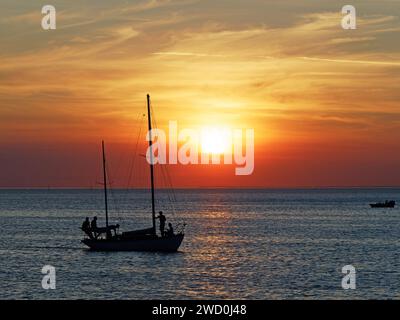 Blick auf einen spektakulären leuchtenden roten Sonnenuntergang mit einer Yacht im Vordergrund, aus Sicht von St Kilda Beach, Melbourne, Australien Stockfoto