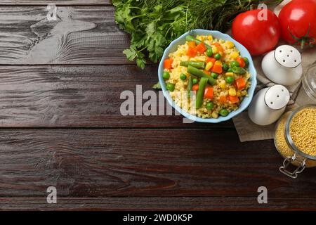 Leckerer Hirsebrei mit Gemüse in der Schüssel und Produkten auf Holztisch, flach gelegt. Leerzeichen für Text Stockfoto