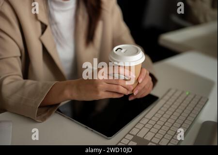 Nahaufnahme einer Geschäftsfrau, die eine Kaffeetasse hält und an ihrem Schreibtisch Kaffee schlürft. Business-People-Konzept Stockfoto