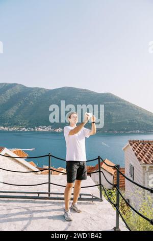 Ein junger Mann macht Fotos mit seinem Handy, während er auf einer Aussichtsplattform am Meer steht Stockfoto