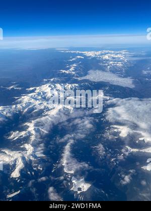 Atemberaubende Luftaufnahme mit schneebedeckten Gipfeln und Wolken über rauem Gelände. Stockfoto