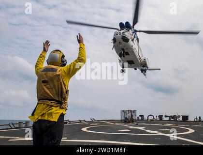Boatswain's Mate Seaman signalisiert einem SA 330 Puma, auf dem Flugdeck der USS Barry zu landen. Stockfoto