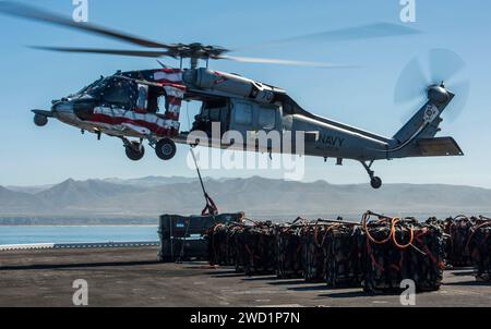 Seeleute befestigen eine Palette von Kampfmitteln an einem MH-60S Sea Hawk an Bord der USS Makin Island. Stockfoto