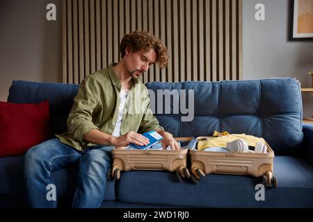 Junger seriöser Mann, der sein Gepäck für die Reise packt und das Ticket in den Koffer packt Stockfoto