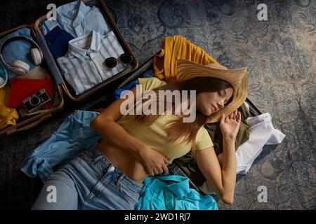 Entspannte Frau, die auf geöffnetem Koffer mit vorbereiteter Kleidung für die Reise liegt Stockfoto