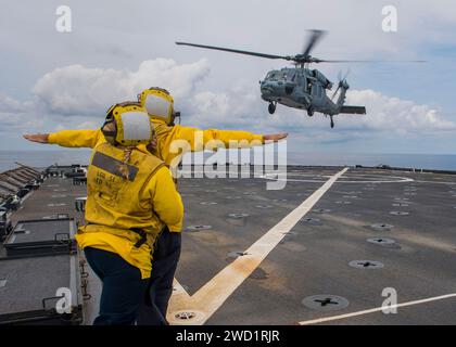 Die Flieger signalisieren einen MH-60S Sea Hawk Hubschrauber, der auf dem Flugdeck der USS Oak Hill landet. Stockfoto