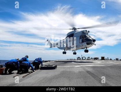 Die Seeleute nehmen Deckung, während ein Hubschrauber der SA-330J Puma auf dem Flugdeck der USS Benfold landet. Stockfoto