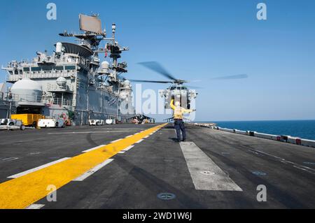 Die Fluggesellschaft Boatswain's Mate signalisiert einen MH-60S Sea Hawk Helikopter, der von der USS America abhebt. Stockfoto