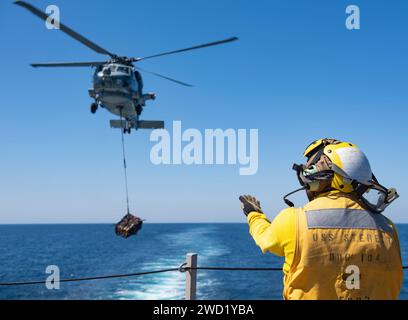 Atswain's Mate signalisiert einem MH-60R Sea Hawk Hubschrauber, Frachtpaletten zu positionieren und abzusenken. Stockfoto