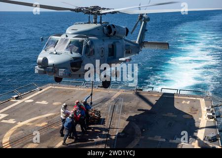 Seeleute befestigen ein Frachtanhänger an einem MH-60R Sea Hawk Hubschrauber auf dem Flugdeck der USS Sterett. Stockfoto